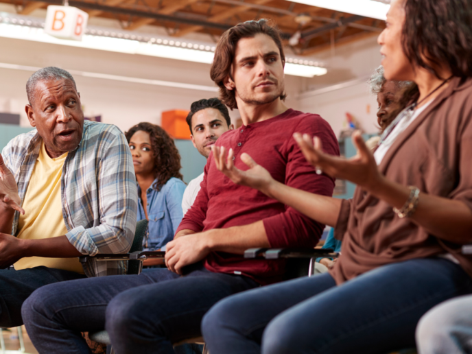 A group discussion between three people at a meeting with others listening - Retrofit West